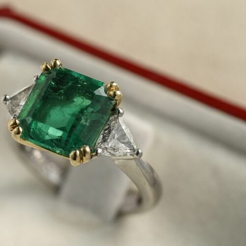 Anello in oro bianco e griffes in oro giallo recante smeraldo di ct. 4,50 e due diamanti taglio triangolo ai lati di ct. 0,30 caduno