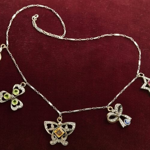 Girocollo in oro bianco con 5 charmes di varie forme in oro e argento, diamanti, granato, tormaline, rubino, zaffiro. Epoca inizi '900