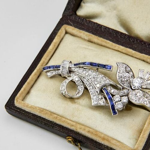 Spilla in oro bianco 18 kt. a tralcio di fiore impreziosita da diamanti di tagli diversi e zaffiri taglio baguette. Epoca anni '30